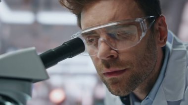 Yakın plan bilim adamı, yenilik laboratuarındaki ilaçları araştırıyor. Gülümseyen profesyonel araştırmacı başarılı bir deney yaptı. Mikroskopta ilaç test tüpü tutan mutlu bir mikrobiyolog.