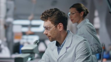 Fen laboratuvarında birlikte çalışan ortaklar bilgisayarı yakından inceliyorlar. Gülümseyen kadın araştırmacı elinde tabletle kimyagerin araştırmasına yardım ediyor. Gözlüklü iki biyolog tıbbi deneyleri tartışıyor..