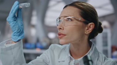 Biyoteknoloji uzmanı test tüpünü yakın tutarak ilaç geliştiriyor. Kadın bilim adamı mikroskopta ilaç örneklerini inceliyor. Gözlüklü kadın kimyager laboratuarda tıbbi araştırma yapıyor..