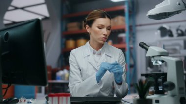 Tıbbi araştırmacı koruyucu gözlük takan bilgisayara benziyor. Beyaz cüppeli kadın bilim adamı biyoteknoloji laboratuvarında çalışıyor. Bilgisayar monitöründen veri okuyan profesyonel bir laboratuar çalışanı