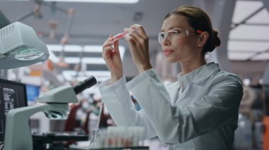 Klinik uzmanı laboratuarda yeni aşıyla test tüpü araştırıyor. Güvenlik gözlüklü ciddi bir kadın bilim adamı mikroskop incelemesi yapıyor. Yenilikçi ilaçlar üzerinde çalışan kadın kimyacı.
