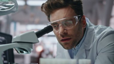 Tıbbi teknisyen mikroskop örneğini inceliyor. Laboratuvarda bilimsel araştırma yapıyor. Hayal kırıklığına uğramış bilim adamı ilaç araştırmasında başarısız oldu. Araştırmacı adam aşı uzmanlığından memnun değil.