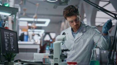 Klinikteki laboratuvarda ilaç deneyleri yapan genç bir mikrobiyolog. Ciddi bilim adamı pipeti mikroskop altında incelemek için kullanıyor. Profesyonel biyoteknoloji uzmanı araştırma yapıyor..