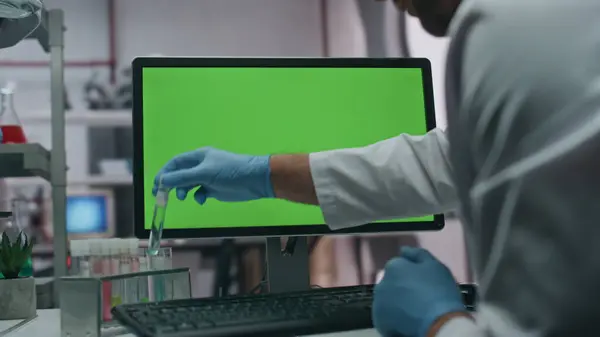 Gloves hands taking test tube entering research data in green screen computer at lab. Closeup unrecognizable doctor working with samples in modern laboratory. Chemist typing on chroma key pc at clinic