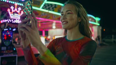 Neşeli genç kayıt cep telefonu videosu kapanıyor. Gülümseyen kız, video çağrısında sosyal medyada yayınlanan akıllı telefonu tutarak lunaparkı aydınlattı. Neşeli kadın yürür lunaparkta fotoğraf çeker