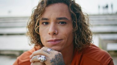 Açık havada gülümseyen hippi görünümlü trend bir adamın portresi. Burnunda piercing olan çekici, kıvırcık bir genç adam. Yakın çekimde poz veriyor. Mutlu dövmeli milenyum modelleri hafta sonu dışarıda dinleniyor.