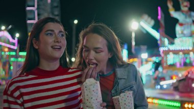 Mutlu arkadaşlar patlamış mısır yiyor, lunaparkta yürüyorlar. Neşeli komik kızlar yaz festivali için atıştırmalık atıyorlar. Neşeli gençler lunaparkta şakalaşıyor. Kadın arkadaşlığı neşesi