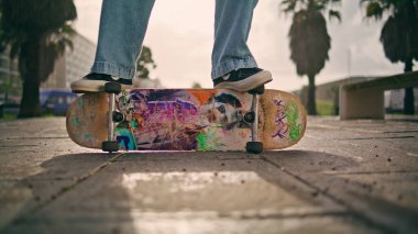 Yakın plan profesyonel kaykaycı Sunny Caddesinde yan patende duruyor. Açık havada hobi olarak tanınmayan genç bir patenci. Asfaltta poz veren bilinmeyen sporcu bacakları..