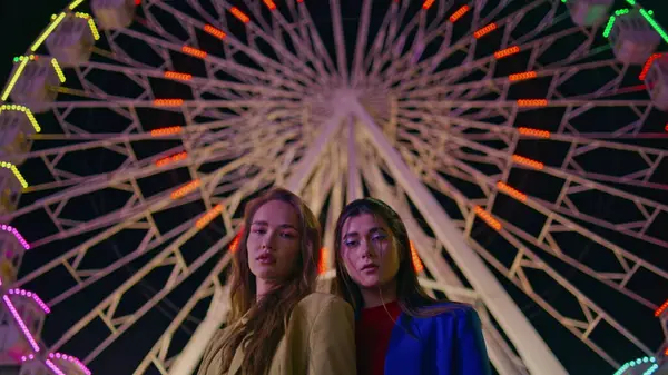 Geceleri panayır atlıkarıncasında poz veren muhteşem mankenler. Ciddi moda kızları akşam karanlığında yanıp sönen renkli dönme dolaba bakıyor. Dinlenen genç kadınlar eğlence parkında dinleniyor..