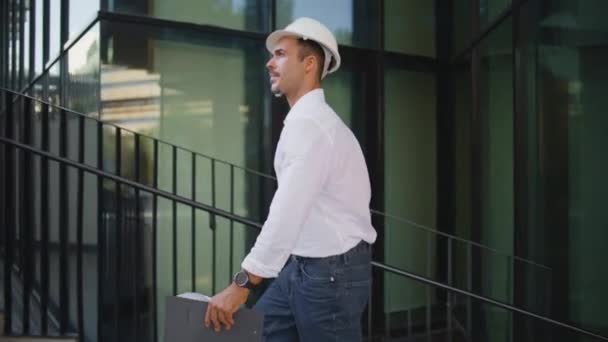 成功的建筑师步行城市举行文件夹特写 一个头戴硬礼帽 长相英俊的拉丁裔男子独自检查建筑物 有信心的工程师在镇上独立工作 带着住宅设计图 — 图库视频影像