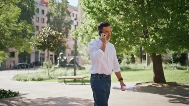 积极的建筑师让手机呼叫步行阳光公园 在绿区外通过电话与轻松的商人进行工作交谈 优雅的男人一个人在街上讲智能手机 — 图库视频影像