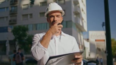 Ciddi mimar, caddeyi kapatırken taşınabilir radyo kullanarak talimatları dikte ediyor. Kasklı, kendine güveni tam bir adam güneşli şehirde telsizle konuşuyor. İspanyol inşaat ustabaşı internetten ayarlamalar yapıyor.
