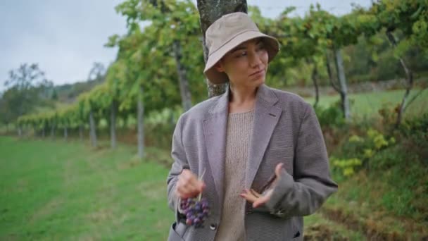 ケアフリーの女性は グリーンブドウ園の景色を近くで見ているブドウを楽しんでいます ハッピーガールは ブドウ栽培の上に立っているおいしいジューシーな果実を食べます 熟した新鮮なグレープバインの収穫を味わうリラックスした女性農家 — ストック動画