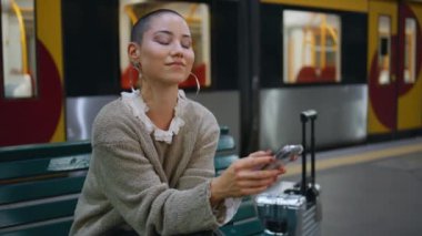Akıllı telefonlara bakan maceraperest bir kadın. Kısa saçlı mutlu kız kürsüde telefon mesajı okuyarak gülüyor. Gülümseyen kadın turist demiryolu taşımacılığıyla seyahat edecek..