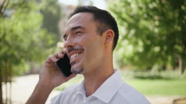 Yazın yeşillik arka planında neşeli bir patron cep telefonuyla konuşuyor. Mutlu gülen adam Sunny Park 'ta iş konularını tartışıyor. İş adamı iş görüşmesinden keyif alan fikirleri öneriyor