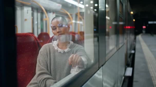 在车站站台的火车窗前 有一个松驰的女人在无聊地望着 可悲的剃光了头的女孩坐在舒适的马车上现代铁路运输 不愉快的乘客等着出发 因旅行而不高兴 — 图库视频影像