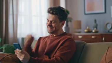 Heyecanlı bir iş adamı cep telefonu ekranında sevinçle seviniyor. Kanepeyi kapatıyoruz. Duygusal adam, akıllı telefon maaş tebligatını evde almayı başarıyor. Mutlu adam sevinçle işaret ediyor