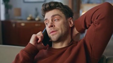 Yakın plan rahatlamış iş adamı, hafta sonu ev içinde cep telefonunu arıyor. Kanepede akıllı telefon siparişi veren yakışıklı adamın portresi. Modern apartman dairesinde cep telefonundan konuşan yorgun adam..