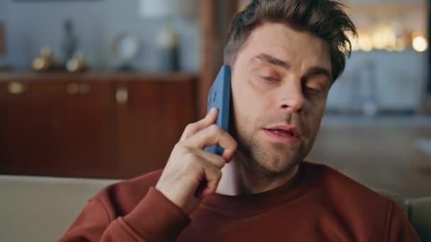 近代的なアパートでスマートフォンを話す心配した男が近づいている 家のソファーに座っている深刻な電話会話を持っている魅力的な男の肖像画 スマートフォン通話で問題を議論する非社交的な男性 — ストック動画
