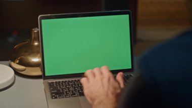 Adam akşam iş yerinde yeşil ekran dizüstü bilgisayarı yazıyor. Ofisteki modern maket bilgisayarını kullanarak çevrimiçi mesajlaşma sunumunda çalışan tanınmayan bir iş adamı. Geç çalışma konsepti