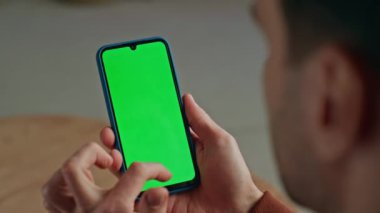Modern iş yerinde yeşil ekranlı, tanınmayan akıllı telefonları kaydıran bir adam. Adam tek başına kroma tuşlu telefona dokunuyor. Bilinmeyen bağımsız görünümlü mobil bankacılık uygulaması evde