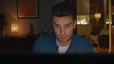 Karanlık Ev 'de dizüstü bilgisayar izleyen ciddi bir çalışan. Odaklanmış yorgun serbest çalışan okuma sunumu teslim tarihi görevlerini çözüyor. Yorgun bir adam gece yarısı çalışıyor. Kaşlarını çatan adam internette sörf yapıyor.