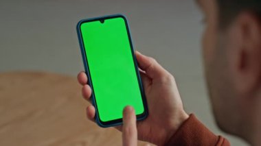 Kapalı alanda yeşil telefon ekranını elle soyan bir adam. Bilinmeyen gevşek adam evde sosyal medyayı kontrol etmek için kromakey akıllı telefon kullanıyor. Anonim serbest çalışan elinde cep telefonuyla takılıyor. 