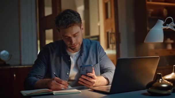 在线经理在深夜的家庭特写笔记 专心致志的男人一个人在晚上的工作场所观看笔记本电脑屏幕视频 一个不修边幅的沉着的家伙在虚拟会议上拿着手机 — 图库视频影像