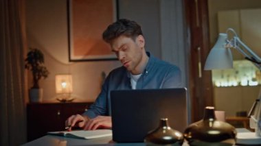 Ciddi bir adam gece evde dizüstü bilgisayar izlerken notlar yazıyor. Odaklanmış muhasebeci cep telefonu kullanarak bütçeyi hesaplıyor. Serbest çalışan adam haftalık rapor hazırlıyor. Akşamları bilgisayara uzaktan bakıyor.