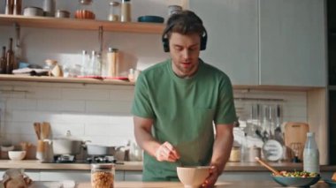 Komik adam kulaklıkla yemek pişiriyor mutfakta dans ediyor. Neşeli, rahat, müzik dinleyen, ev mutfağında kablosuz kulaklık takan bir adam. Yakışıklı meloman lezzetli bir kahvaltı hazırlıyor.