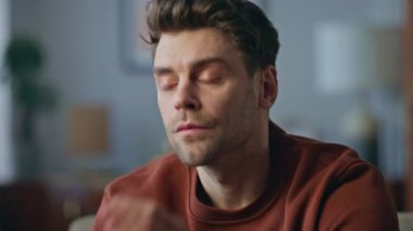 Düşünceli bir adam modern oturma odasında oturuyor. Yakın plan. Çekici, ciddi bir adamın tek başına karar verme sorununu düşünen portresi. Kaygılı yakışıklı erkek koltukta dinleniyor yalnızlık hissediyor