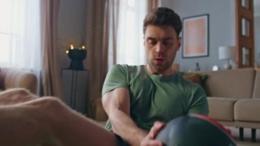 Yakışıklı bir sporcu evde top ile karın kaslarını çalıştırıyor. Modern oturma odasında karın kasları için egzersiz yapan odaklanmış aktif sporcu. Genç formda adam yerde spor antrenmanı yapıyor.