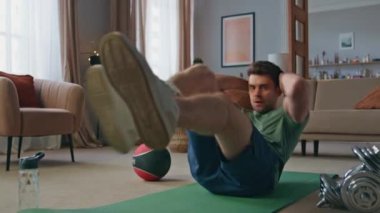 Spor spikeri oturma odasında karın kaslarını çalıştırıyor. Gergin genç sporcu karın kasları için spor egzersizleri yapıyor dayanıklılık. Sağlıklı vücut için evde çalışan güçlü bir adam..