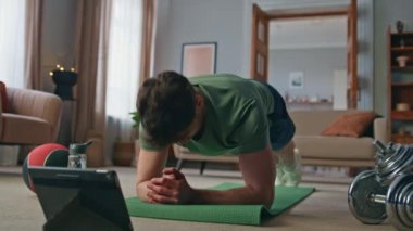 Atletizm, yoga minderinde ayakta duran online ders tahtası pozisyonunu takip ediyor. Tablet üzerinde kas egzersizi yapan sporcu. Aktif sporcu bilgisayar eğitimi ile egzersiz yapıyor..