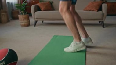 Erkek bacakları paspasın üstünde ev oturma odasına zıplıyor. Enerjik sporcu günlük antrenmanlarda vücut dayanıklılığı eğitimi alıyor. Sağlıklı formda sporcu dairede kardiyo egzersizi yapar. Vücut ağırlığını kontrol eden aktif adam