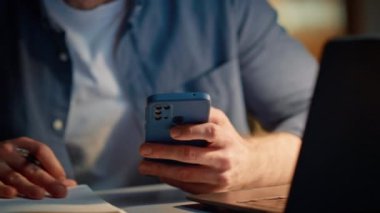 Akşam evindeki cep telefonunu hesaplayan geç muhasebeci elleri. Neşeli gülen adam dizüstü bilgisayar ekranında gülümseyen bir videoyla konuşuyor. Evde elinde akıllı telefon tutan mutlu adam bilgisayardan konuşuyor.