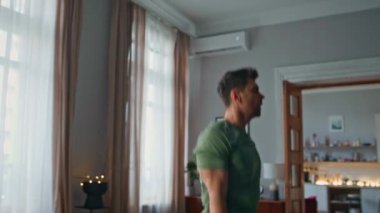 Oturma odasına atlayan zinde bir adam, yakın mesafeden spor yapıyor. Genç enerjik sporcu günlük antrenmanlarda kardiyo egzersizleri yapıyor. Sağlıklı genç adam evde kas çalıştırıyor. Sporcu rutini.