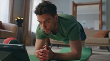 Atletizm sporcusu oturma odasında tabletle video öğretiyor. Çevrimiçi spor paspası dersleri izleyen yakışıklı bir adam. Formda sporcu antrenmanda internet koçunu takip ediyor..
