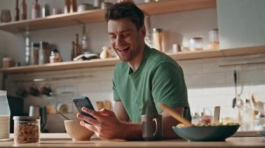 Neşeli bir adam mutfak tezgahında kahvaltı ederken akıllı telefonuyla gülüyor. Gülümseyen yakışıklı adam cep telefonunda komik videolar izliyor. Rahat bir hipster cep telefonuna bakıyor.