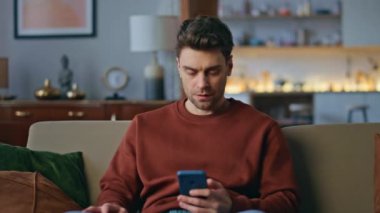 Hayal kırıklığına uğramış serbest çalışan daire kanepesinde akıllı telefon mesajı okuyor. Cep telefonu e-postasıyla duygusal olarak tatmin olmayan endişeli bir adam. Cep telefonu ile hayal kırıklığına uğramış adam iş krizi yaşıyor..
