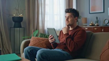 Rahat müşteri görünümlü tablet koltukta rahat bir oturma odası. Evde internetten alışveriş yapan yakışıklı bir adam bilgisayarını araklıyor. Dijital cihaz kullanarak sosyal medyayı izleyen tıraşsız adam..
