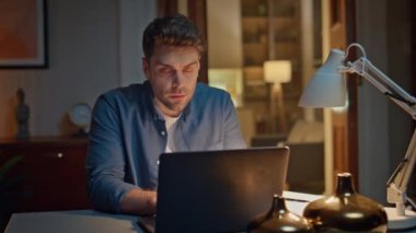 Odaklanmış adam Dark Home 'da internette internette geziniyor. Modern dairede dizüstü bilgisayarda klavye yazan yakışıklı genç adam. Bilgisayarı kullanarak online sipariş veren çok düşünceli bir müşteri.