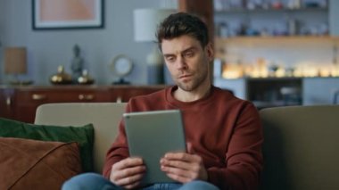Düşünceli iş adamı tablet web sitesine göz atıp kanepeyi kapatıyor. Kanepedeki bilgisayar ekranına bakarak ciddi anlamda çekici bir adam düşünüyor. Düşünceli çevrimiçi yönetici dairede uzaktan çalışıyor..