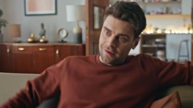 Modern dairede rahat hipster kanepe düşüşü cep telefonuyla yakın çekim. Çekici gülümseyen adam akıllı telefon ekranına bakıyor ve evden mesaj alıyor. Hafta sonu dinlenirken cep telefonu kullanan traşsız adam.