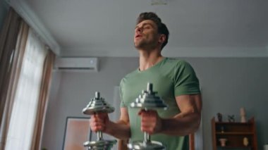 Ev antrenmanında el sıkışan bir adam. Motive olmuş güçlü bir sporcu, halterleri kaldırıyor, oturma odasında pazıları eğitiyor. Formda sporcu, kas gücü için spor yapıyor..