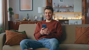 Gülümseyen öğrenci rahat koltukta akıllı telefon sosyal ağlarına göz atıyor. Mutlu, rahat bir adam cep telefonu ekranında evde dinleniyor. Telefondan komik videolar izleyen yakışıklı adam..