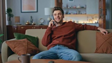 Dinlenen adam rahat oturma odasındaki kanepede akıllı telefonla iletişim kuruyor. Gülümseyen yakışıklı adam hafta sonu cep telefonu paylaşımından bahsediyor. Mutlu hipster kanepede dinleniyor. Keyifli sohbetler..