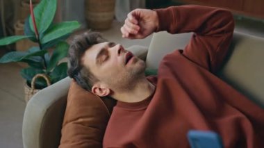 Yorgun adam işten sonra kendini yorgun hissedip kanepeye düşüyor. Endişeli adam akıllı telefon ekranına bakıp kötü haberleri okuyor. Cep telefonuyla şaşkına dönmüş erkek rahat bir oturma odasında dinleniyor..