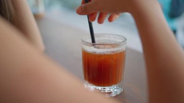 Caddedeki kafede saman gibi soğuk bir kokteylden içen tanınmamış bir kadın. Ahşap masada buz küpleriyle el çırpan kız içeceği. Genç restoran ziyaretçisi yalnız başına alkolün tadını çıkarıyor..