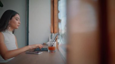 Kafeteryada çalışan Asyalı serbest çalışan panoramik pencereyi kapatın. Kafe masasında tek başına oturan odaklanmış iş kadını dizüstü bilgisayarı. Güzel kız uzaktan çalışan internetteki interneti kullanarak sörf yapıyor..